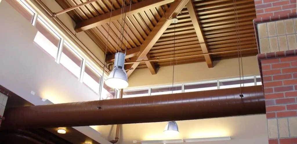 The ceiling of a building with wooden beams and pipes.